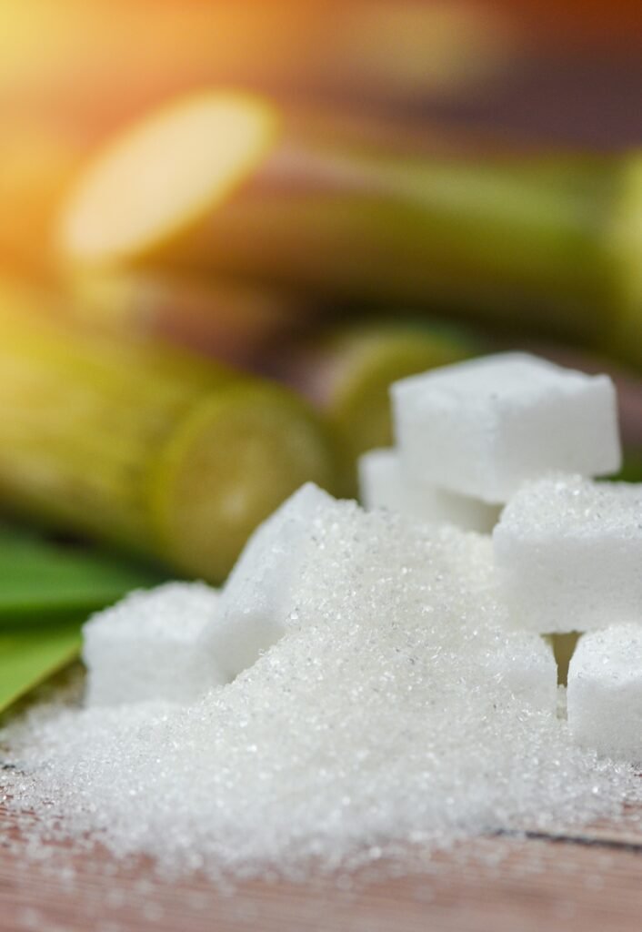 White sugar cubes and sugar cane on wooden table and nature background
